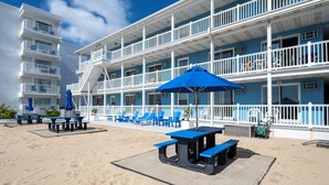 A beachfront hotel with multiple balconies, outdoor seating, and a sandy beach area. - Oceanfront condos with 3 night minimum rentals and linens included! (Ocean City)