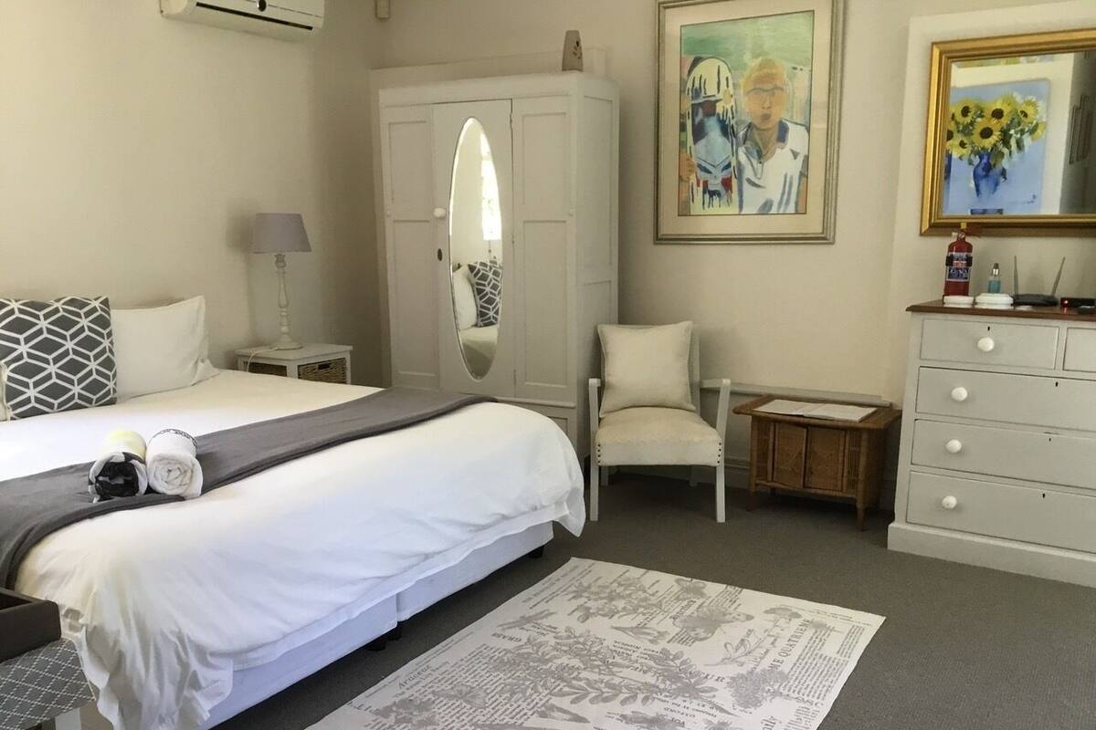 A hotel room with a bed, a chair, a dresser, a mirror, and a painting on the wall.