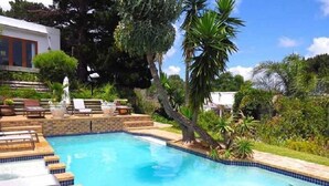 A swimming pool with lounge chairs and a small waterfall feature. - Ocean Golf Guest House (Cape Town)