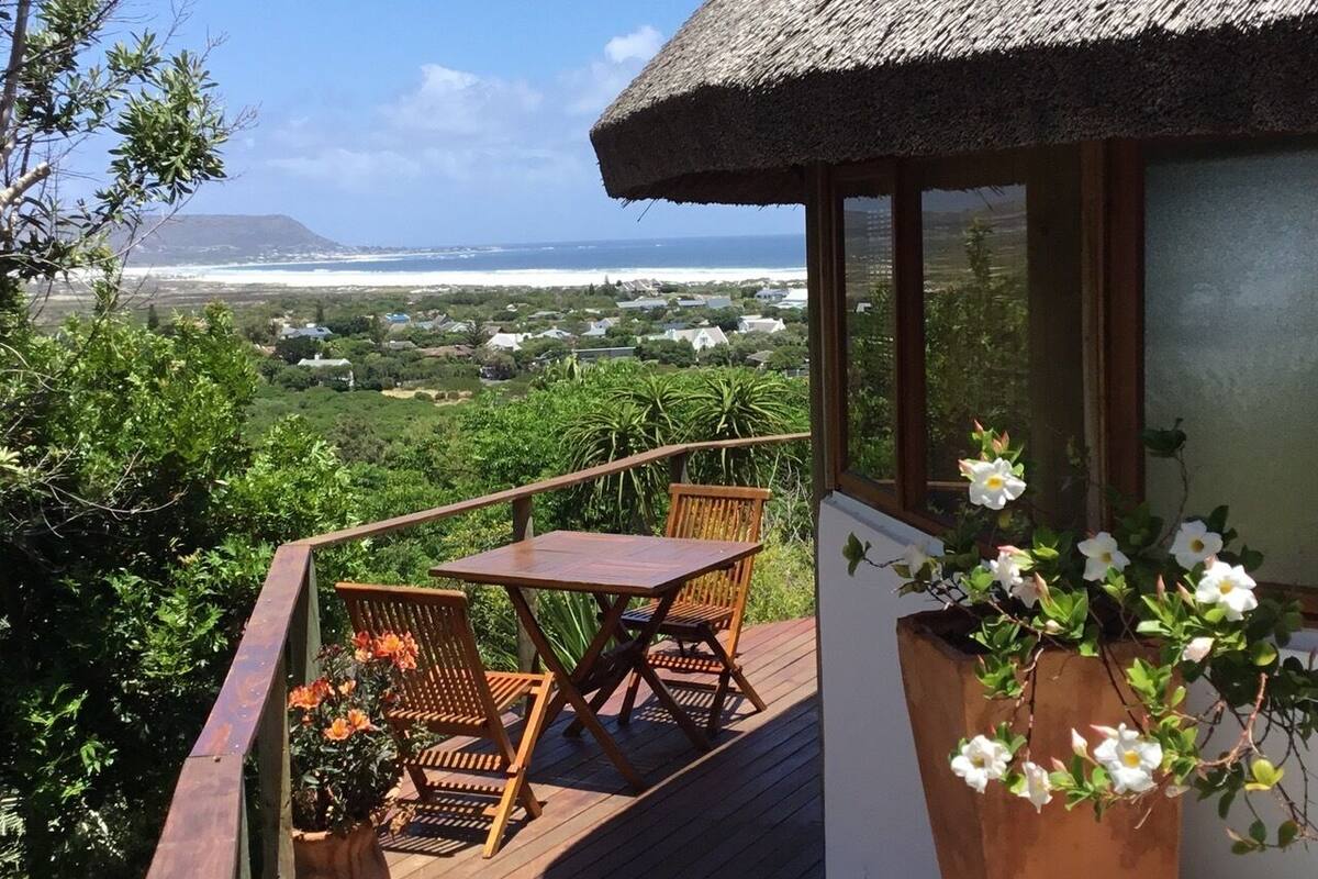 A wooden deck with a table and chairs, overlooking a coastal landscape with a view of the sea and a mountain in the distance.
