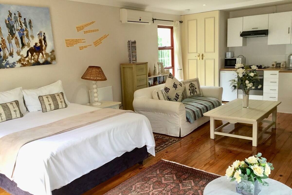 A bedroom with two beds, a sofa, a coffee table, and a kitchen area visible through an open door.
