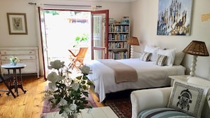 A bedroom with a bed, a white sofa, a coffee table, a bookshelf, and a door leading to a balcony. - Ocean Golf Guest House (Cape Town)