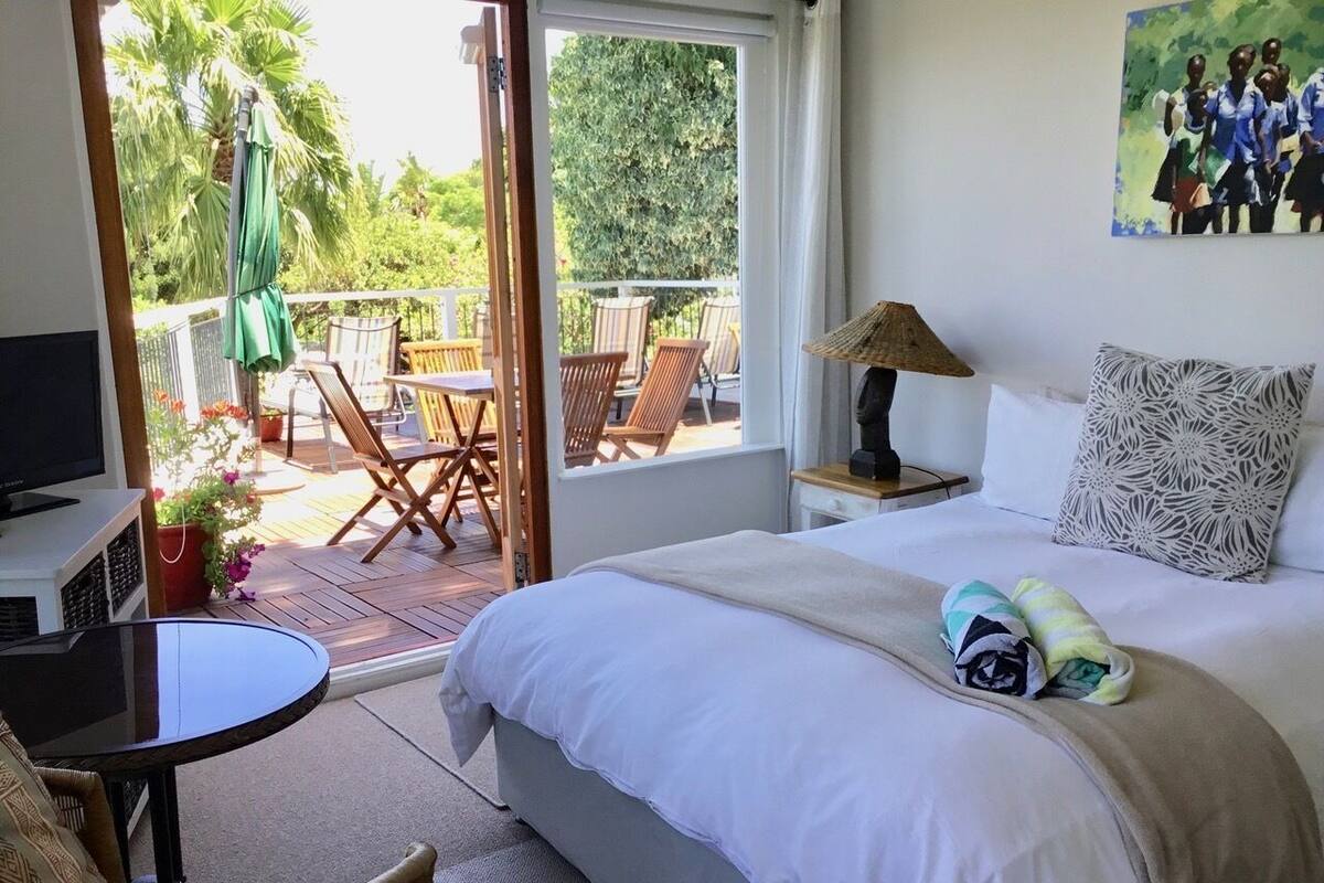 A bedroom with a bed, a television, a table, and a balcony with chairs and a table.