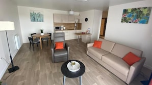 A modern living room with a sofa, a coffee table, and a dining area with chairs. - Domitys Les Rives du Cher (Montlucon)