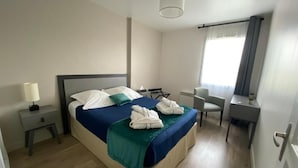 A hotel room with a bed, bedside table, desk, chair, and a window with curtains. - Domitys Les Rives du Cher (Montlucon)