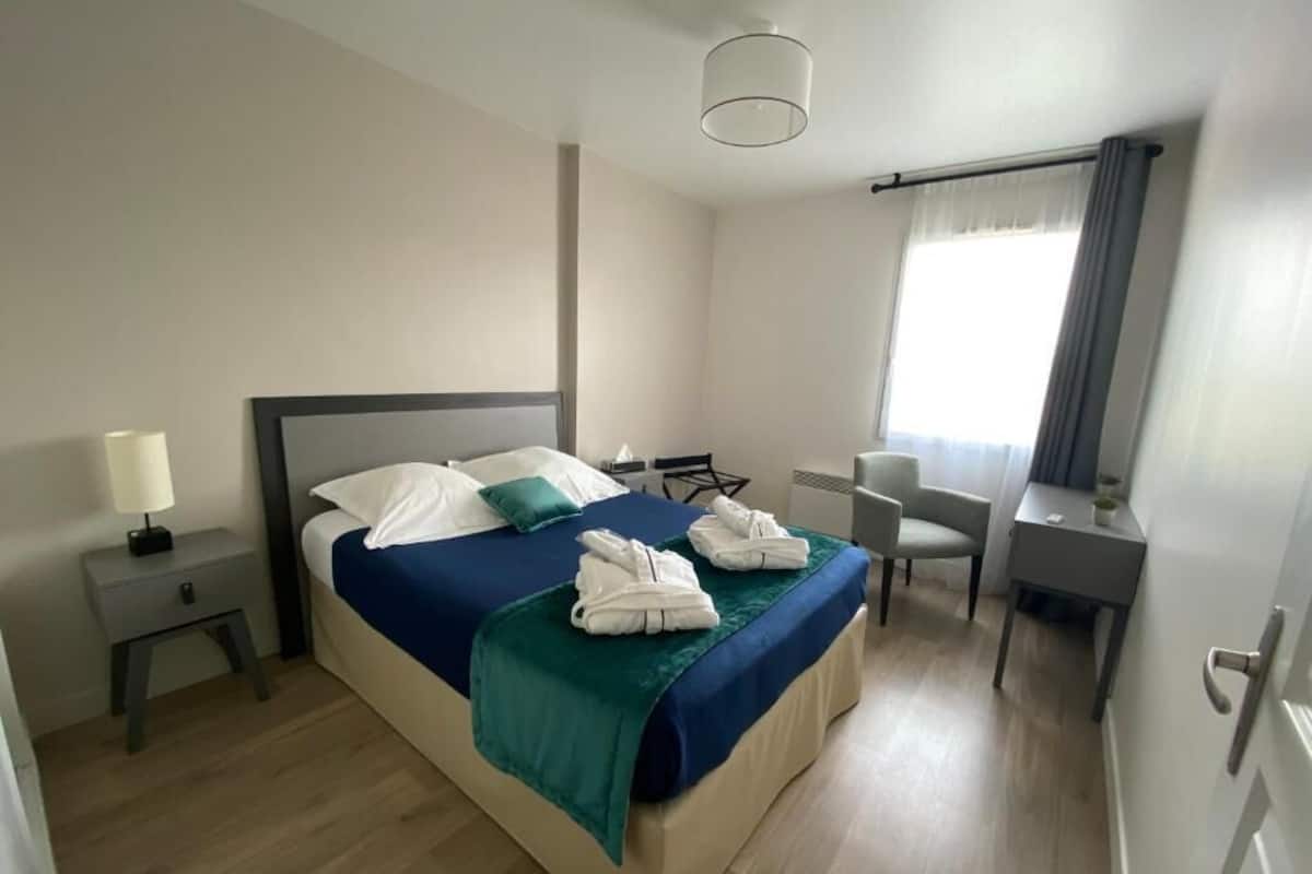 Habitación de hotel con cama, mesita de noche, escritorio, silla y ventana con cortinas.