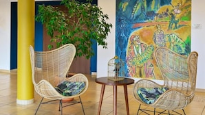 A lobby with wicker chairs, a round table, and a large abstract painting. - Domitys Les Rives du Cher (Montlucon)