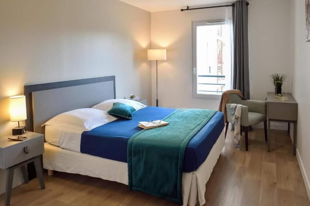 Un dormitorio ordenado con cama, lámparas de noche, un escritorio y una silla.
