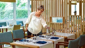 A restaurant with wooden slat partitions, tables set with blue napkins, and a person serving. - Domitys Les Rives du Cher (Montlucon)