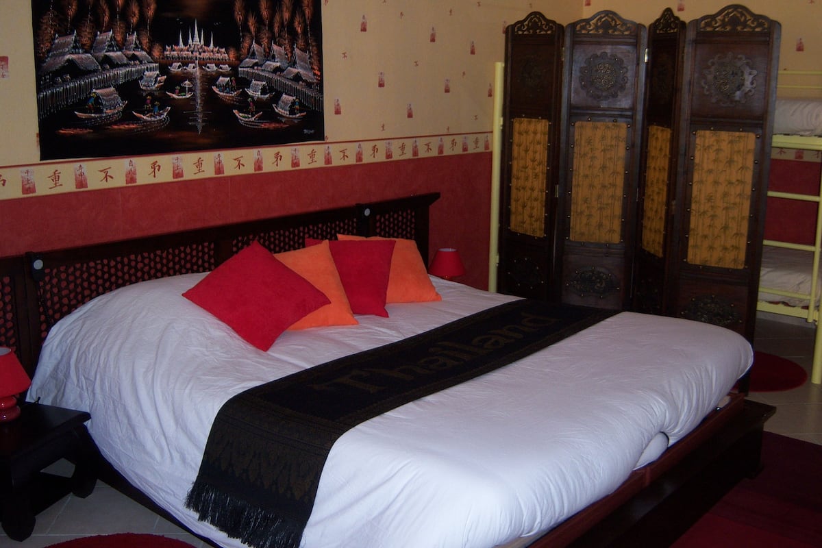 A bed with a red and orange headboard, a black throw blanket, and a painting of boats on the wall.