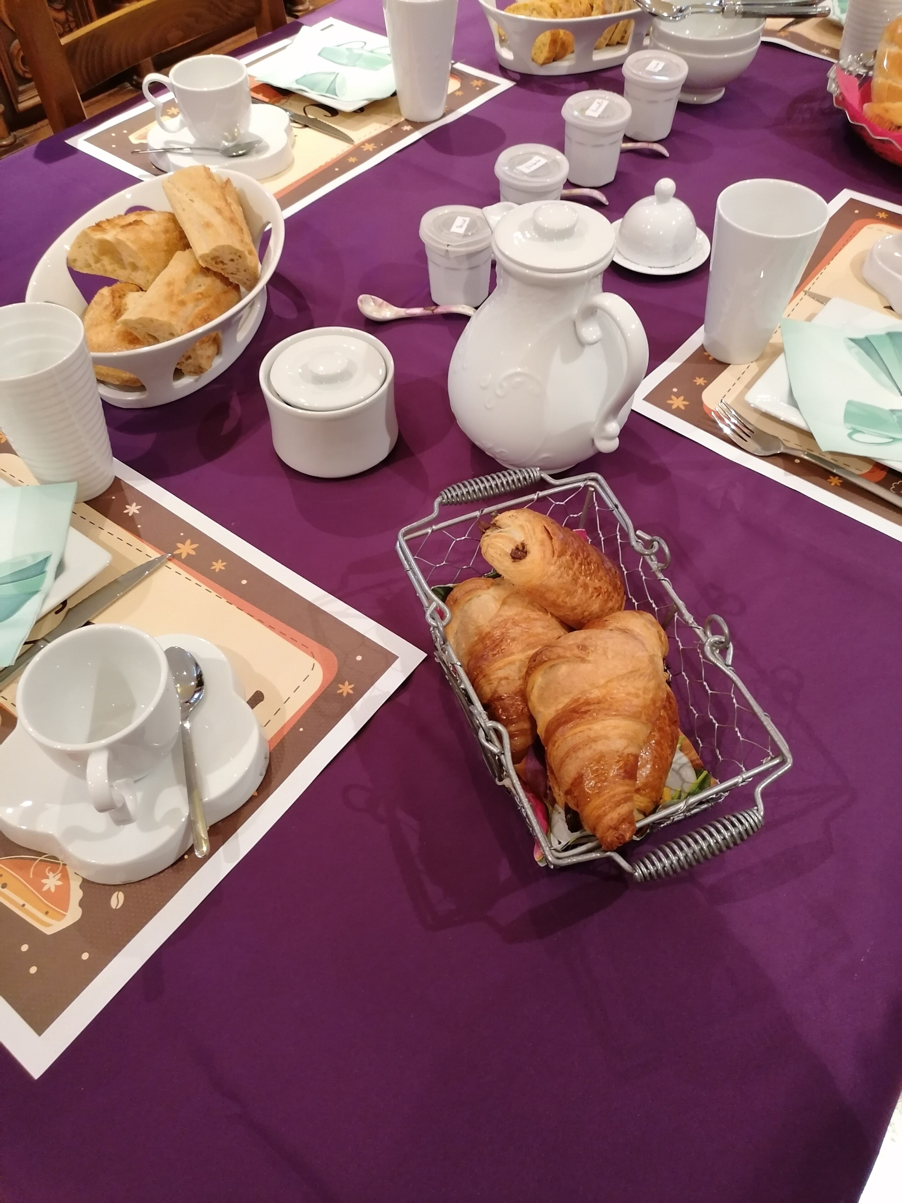 Une table de petit-déjeuner avec des croissants, des théières, des tasses et des soucoupes.