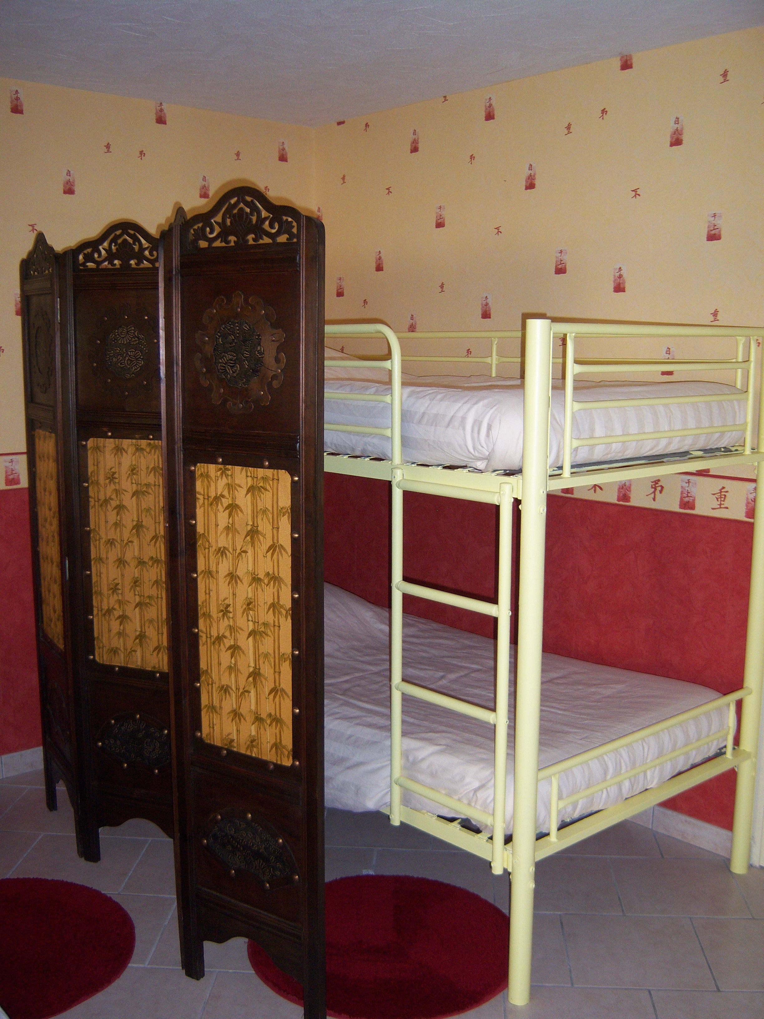 Een kamer met stapelbedden, een klassiek houten kastje en behang met een patroon.