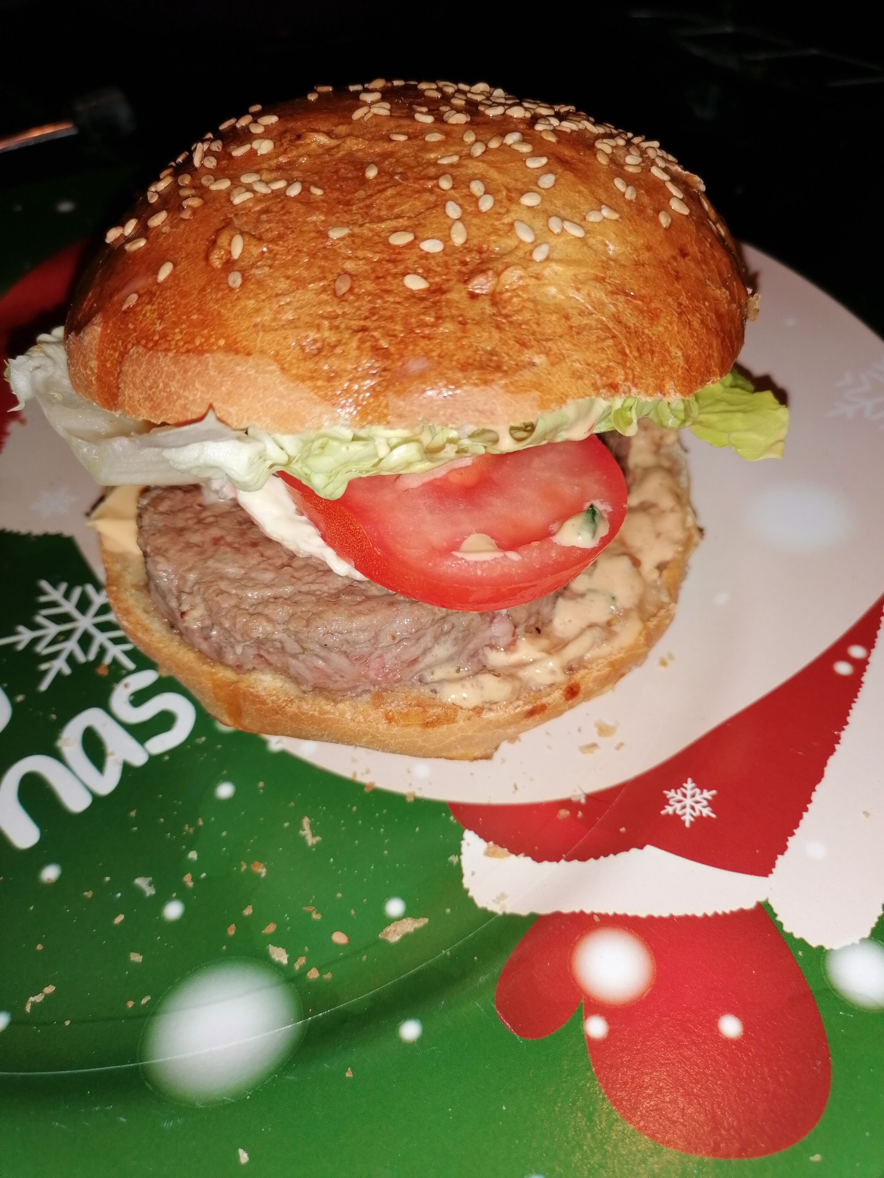 A hamburger with lettuce, tomato, and a sesame seed bun on a plate.