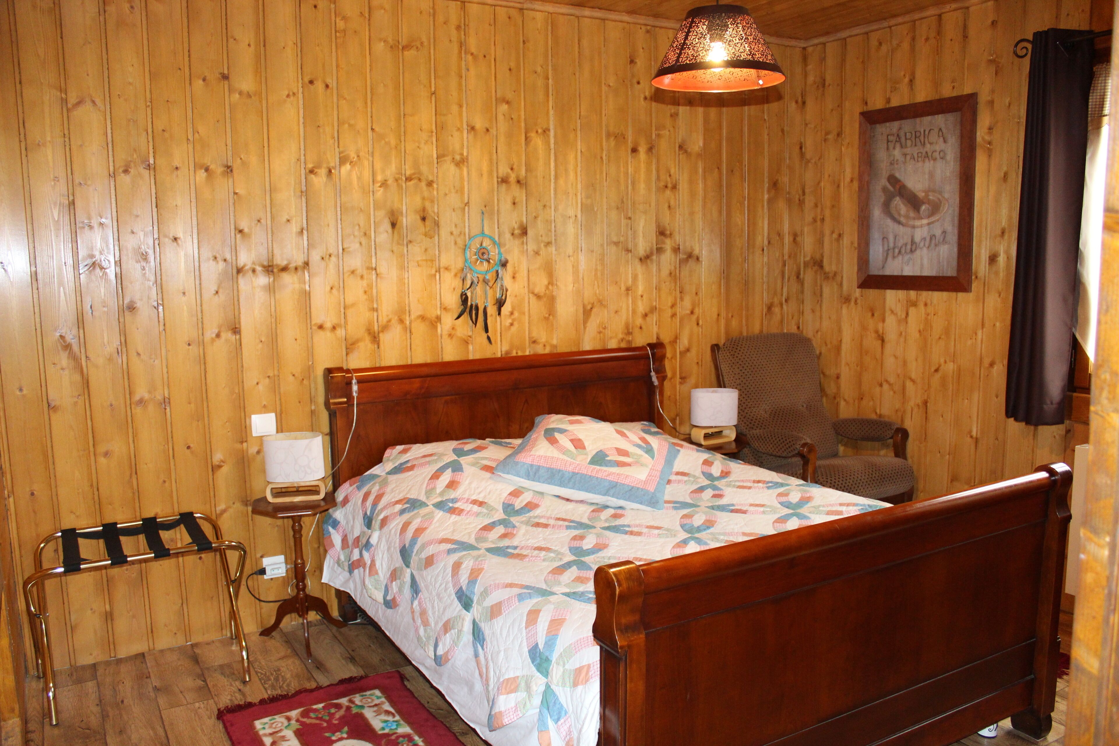 Een kamer met houten lambrisering, een bed, een stoel, een nachtkastje en een dromenvanger aan de muur.