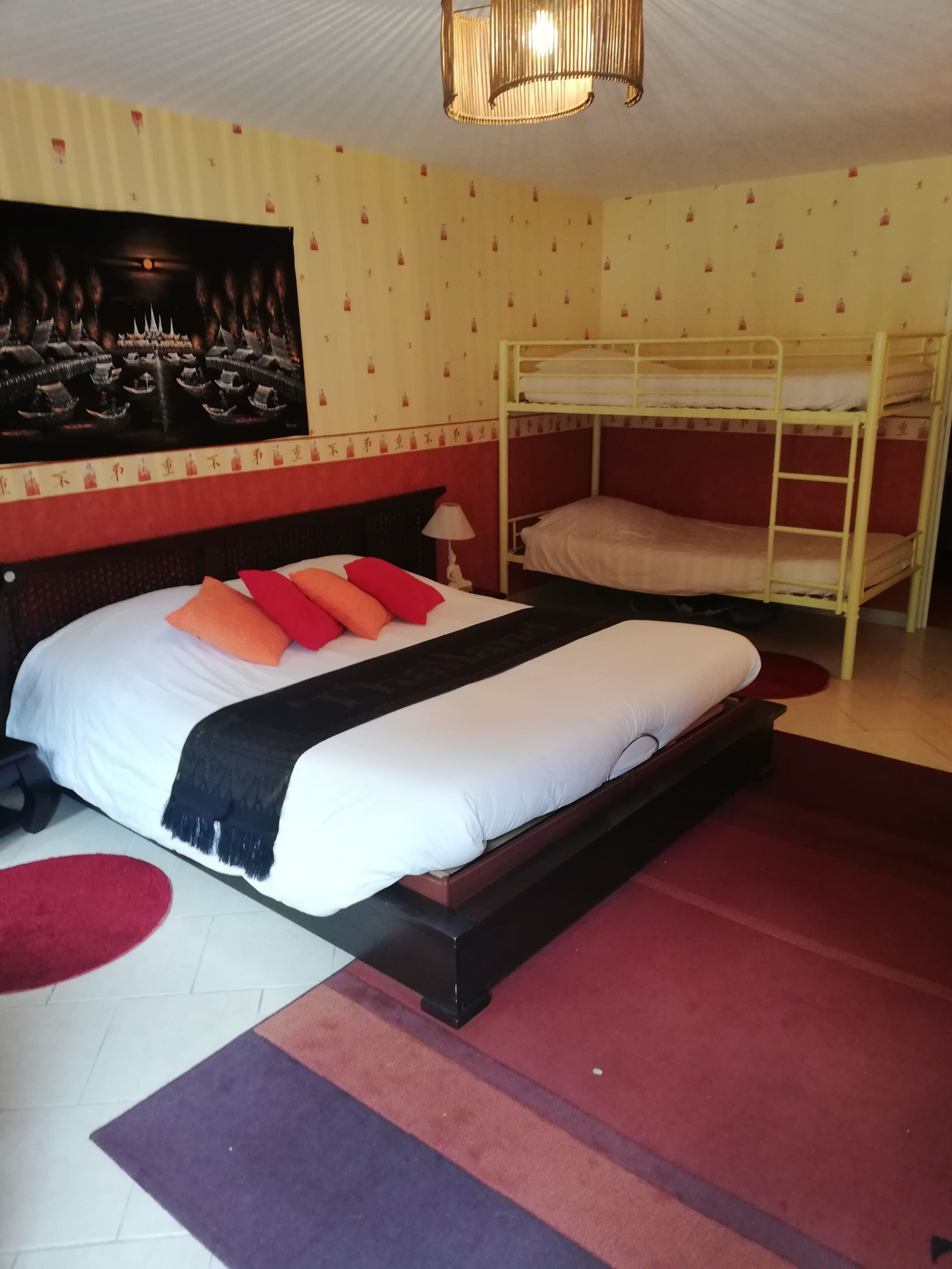 A hotel room with a large bed, a bunk bed, a red carpet, and a wall with a patterned design.