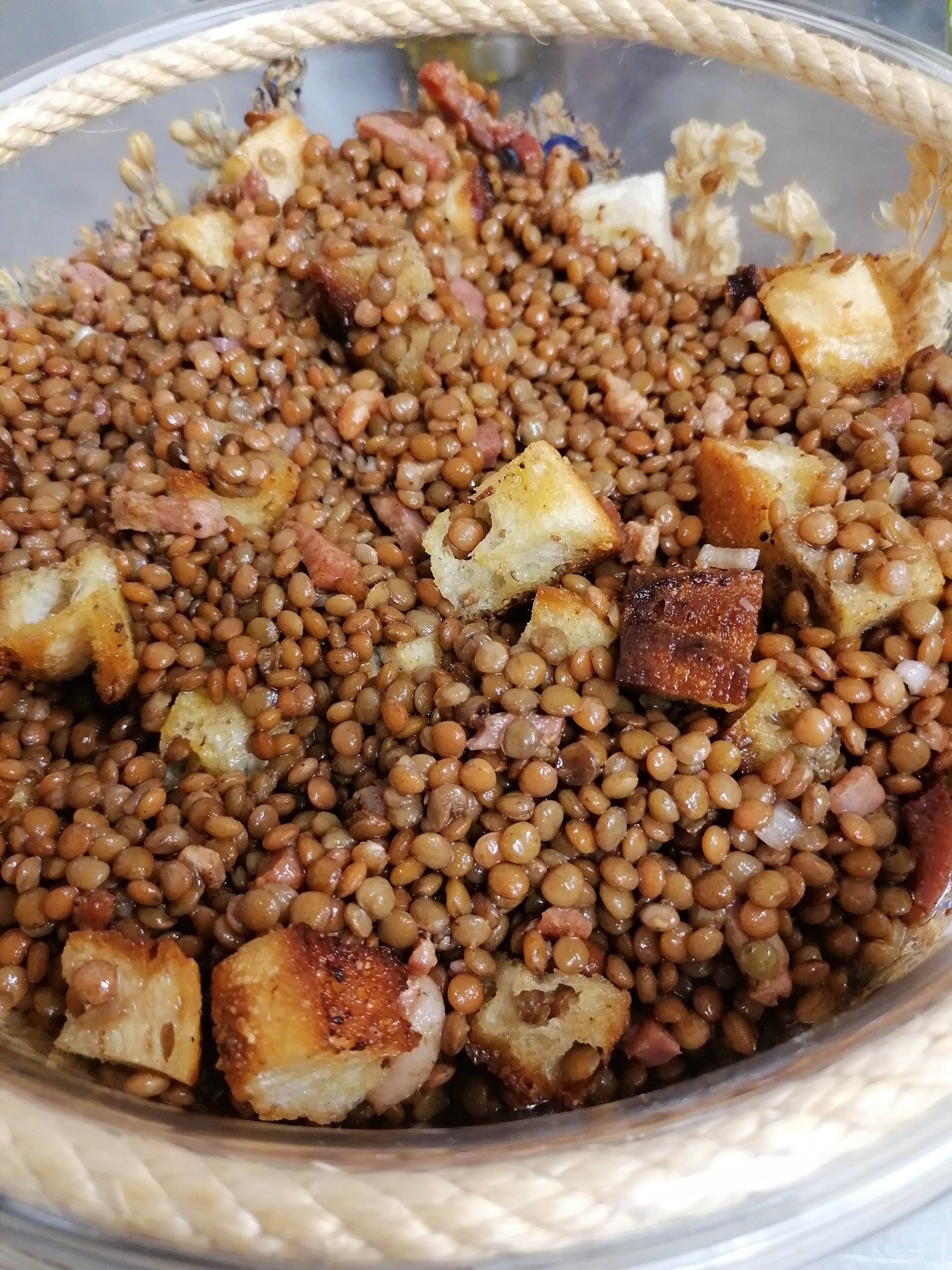 A bowl of lentils with diced potatoes and pieces of meat.
