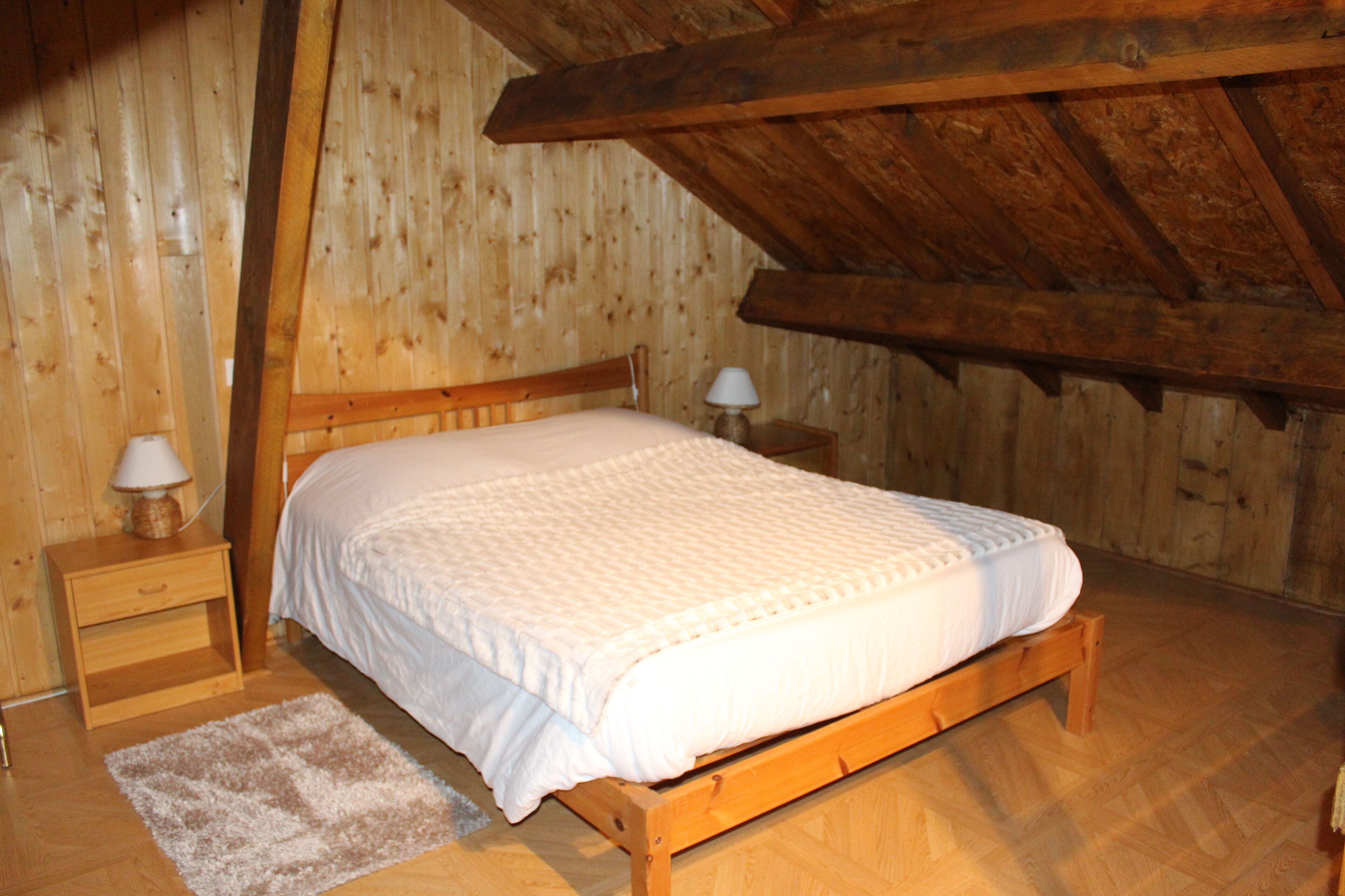 A wooden-framed bedroom with a bed, nightstands, and a rug.