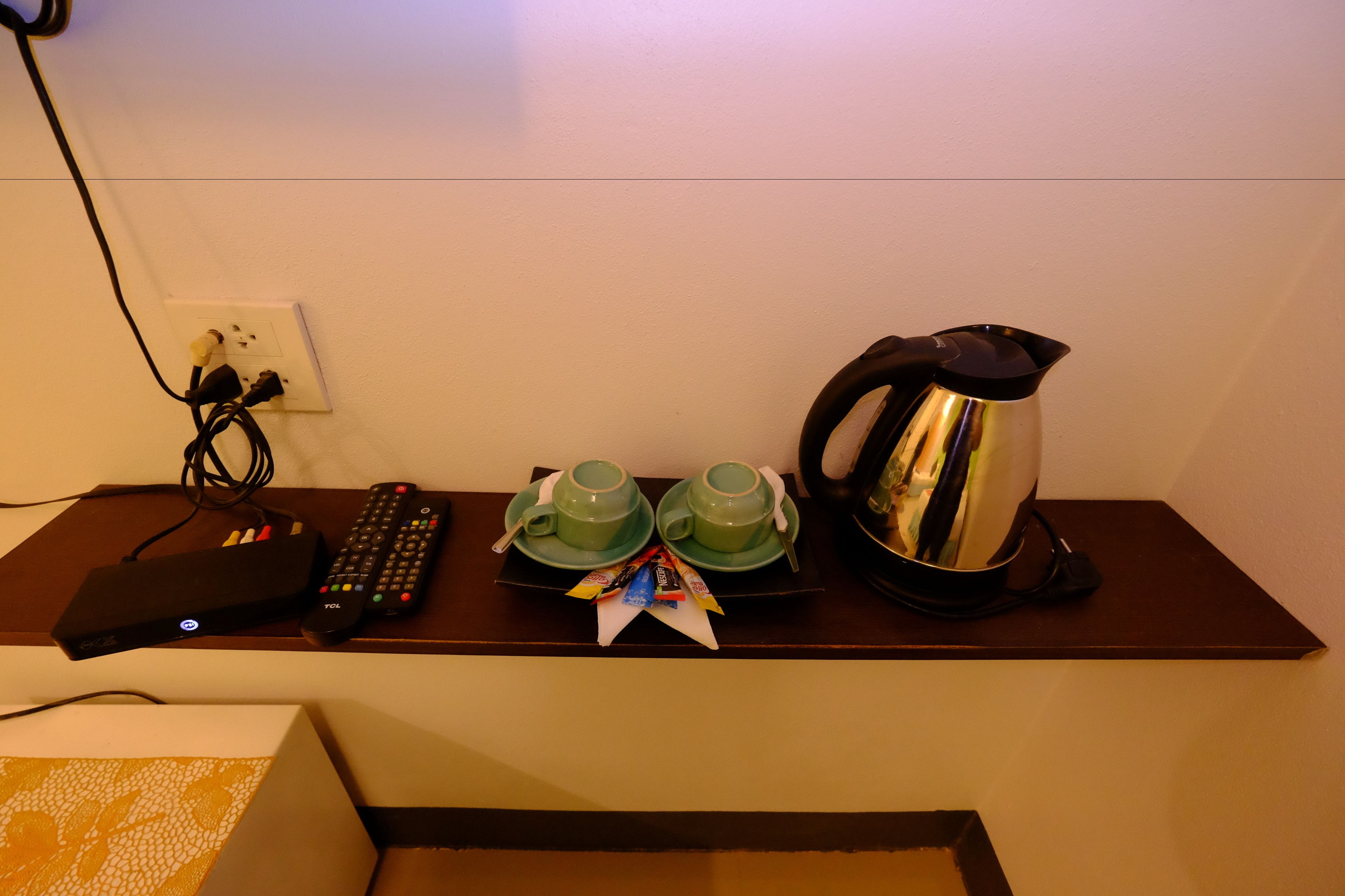 A shelf with a remote control, two green cups, a kettle, and a box.