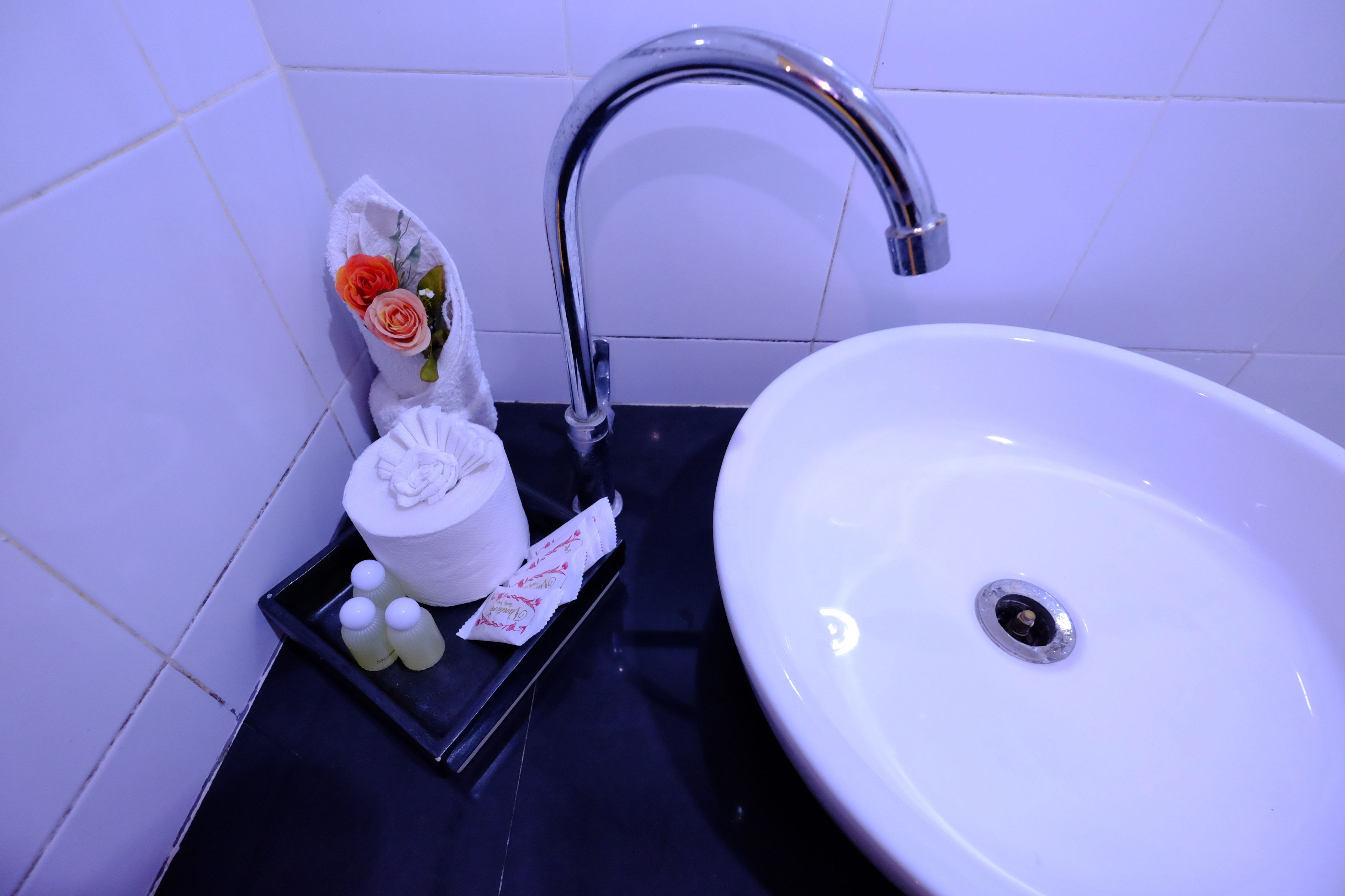 A bathroom sink with a chrome faucet, a white basin, and toiletries including a towel, a bottle, and a small container.
