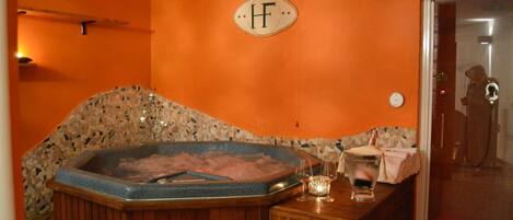 A spa area with a hot tub, wooden benches, a towel rack, and a glass door leading to a shower area.