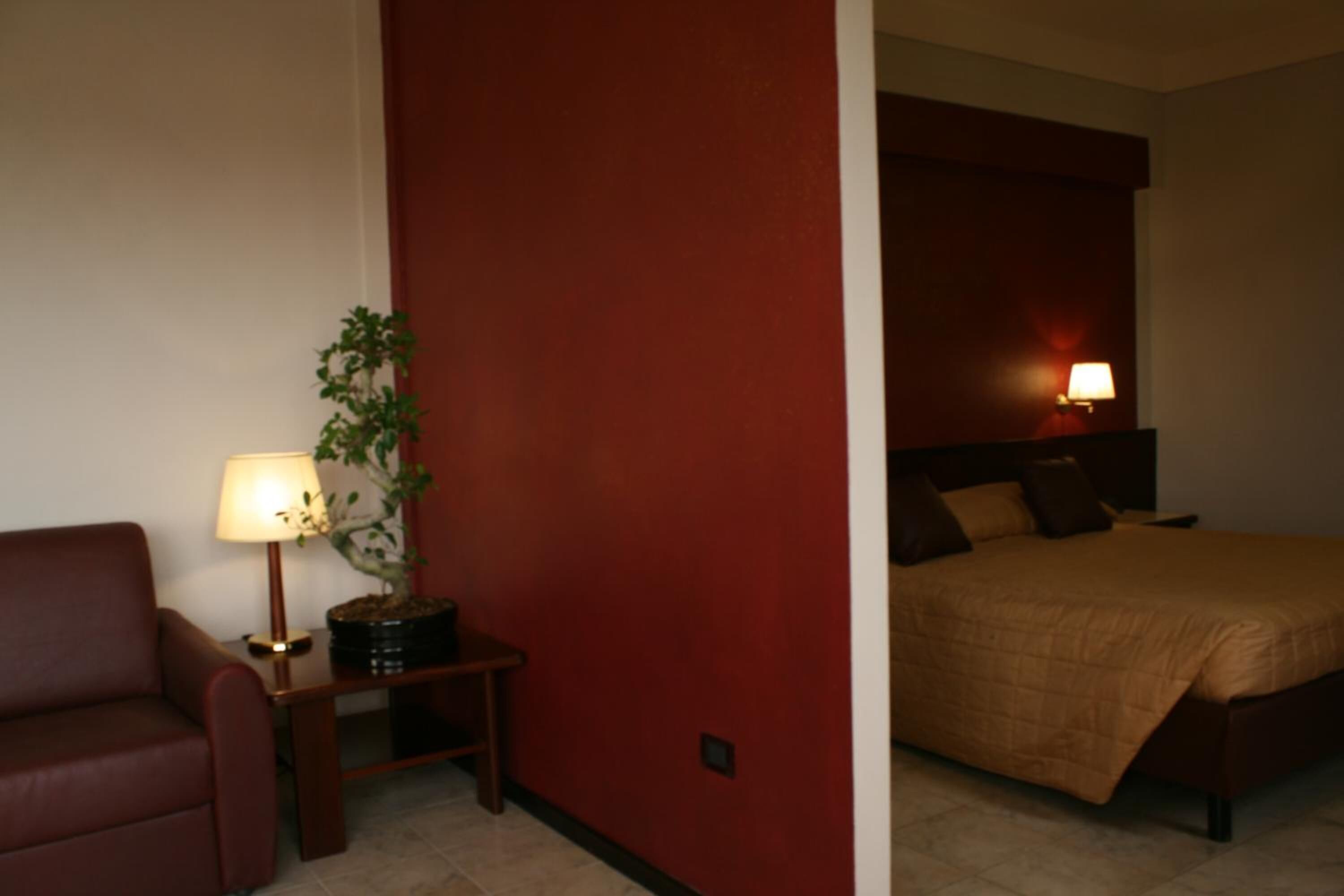 Una camera d'albergo con un letto, un comodino con una lampada, una pianta in vaso e una parete decorata in rosso.