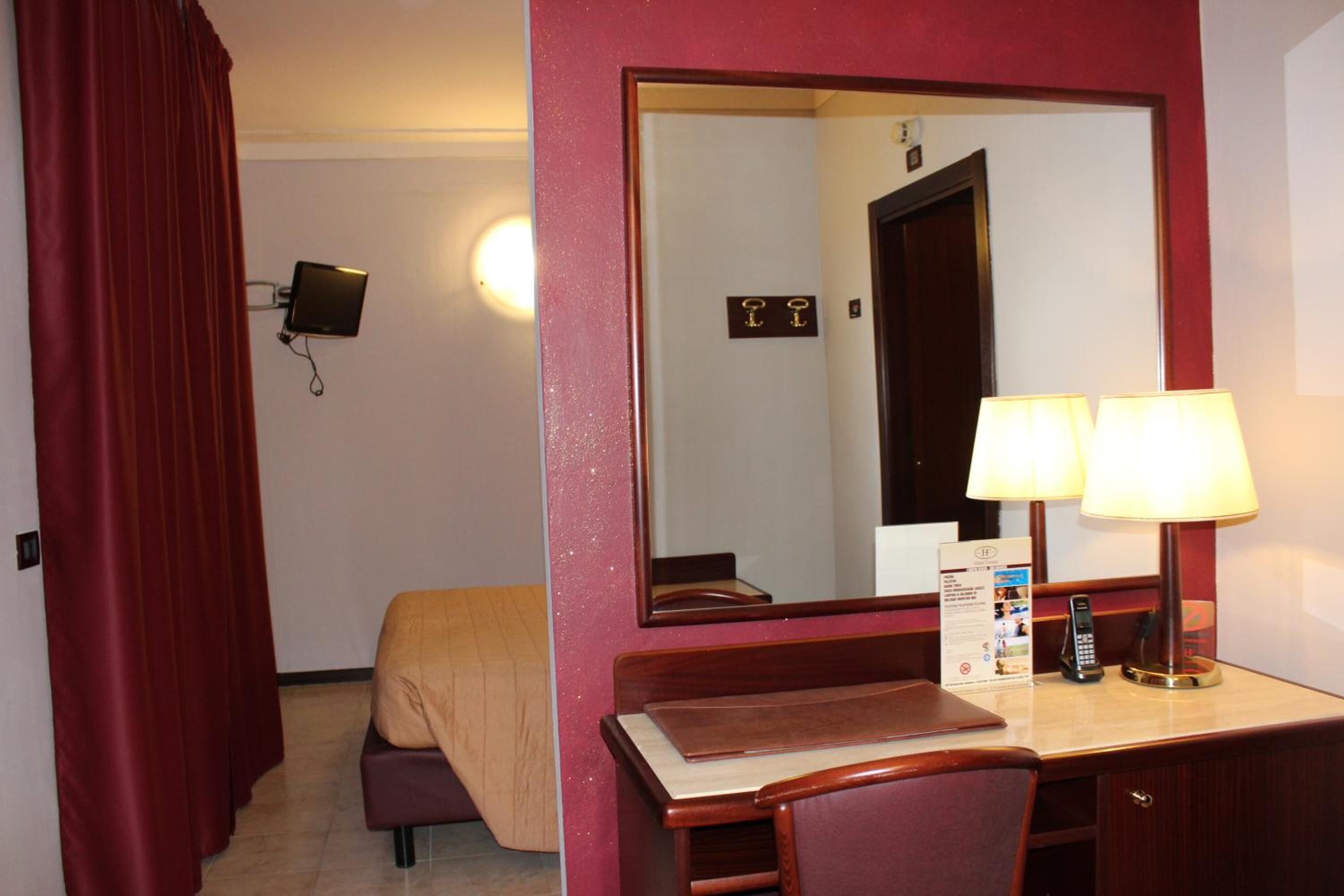 Une chambre d’hôtel avec un lit, un bureau doté d’une lampe, un téléphone et un miroir.