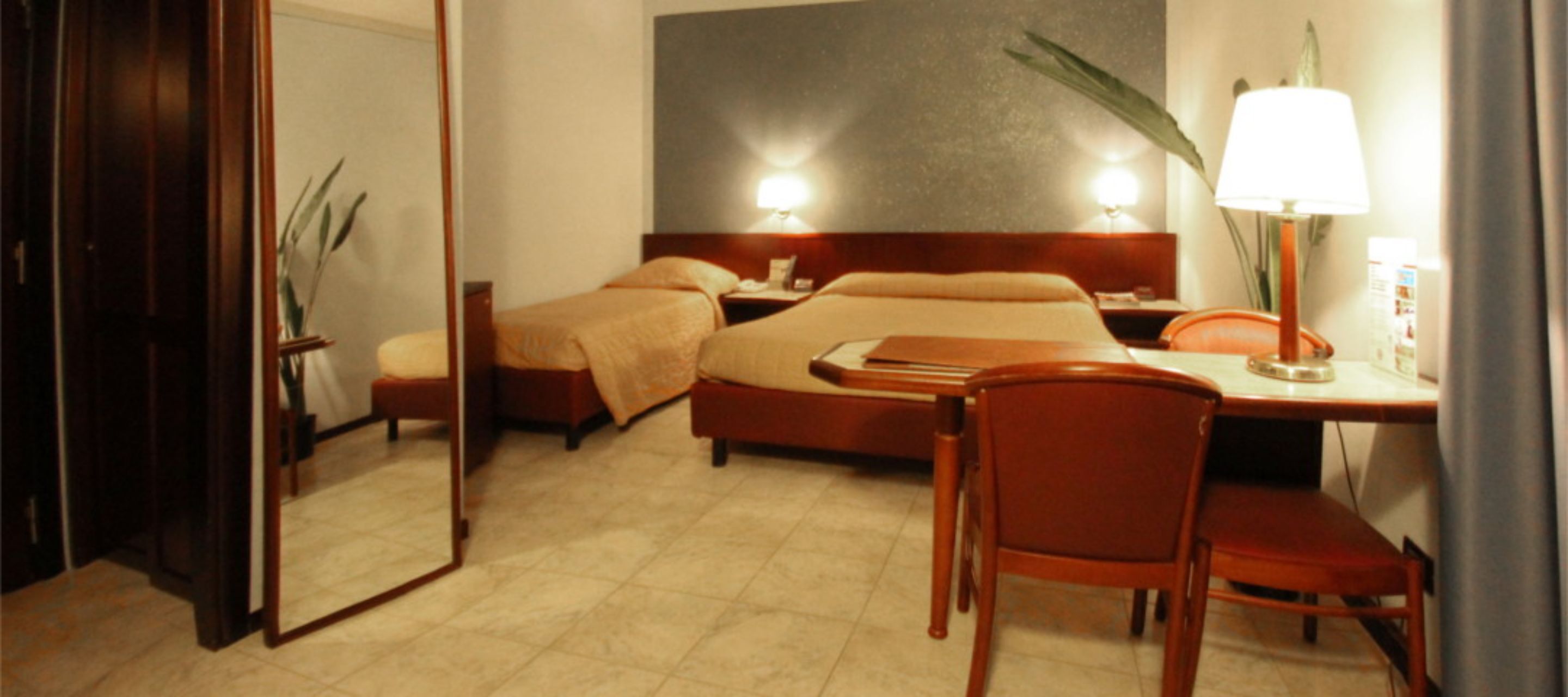 Ein Hotelzimmer mit Bett, Nachttisch, Lampe, Stuhl und einem großen Spiegel.