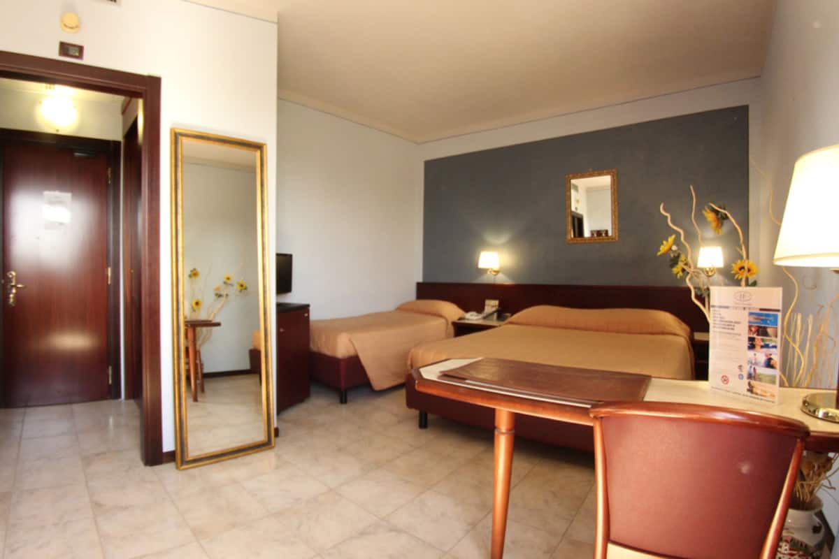 A hotel room with a bed, a desk, a chair, a mirror, and a nightstand.