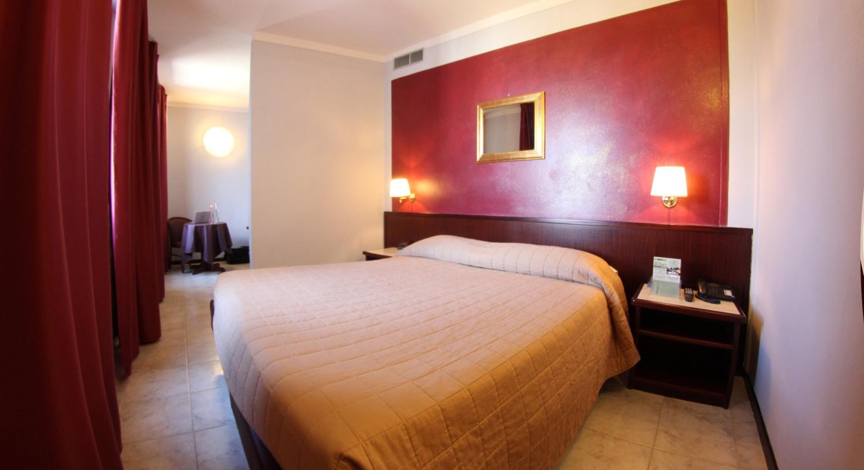 Camera d'albergo con un letto grande, due abat-jour, un comodino e una parete decorata di rosso.