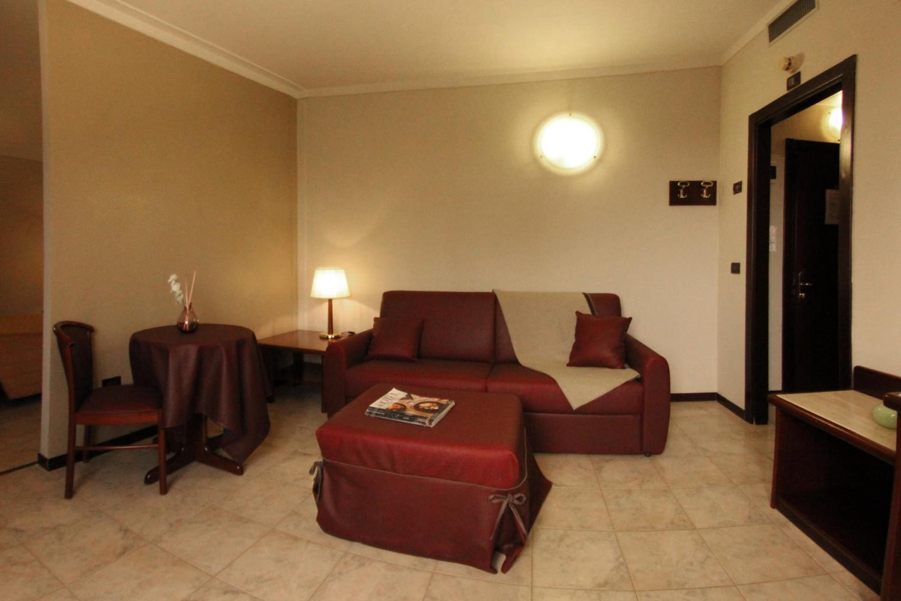 Una sala de estar compacta con un sofá, un reposapiés y una mesita de noche con una lámpara.
