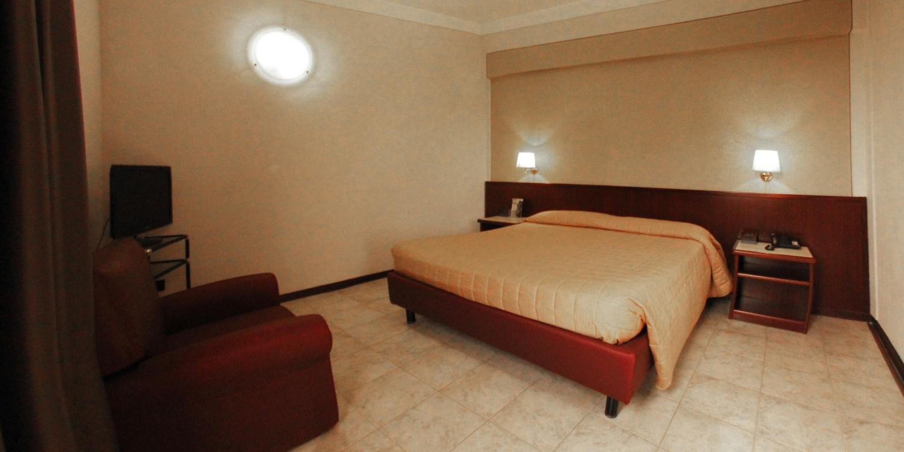 A hotel room with a bed, a chair, a desk, and a television.