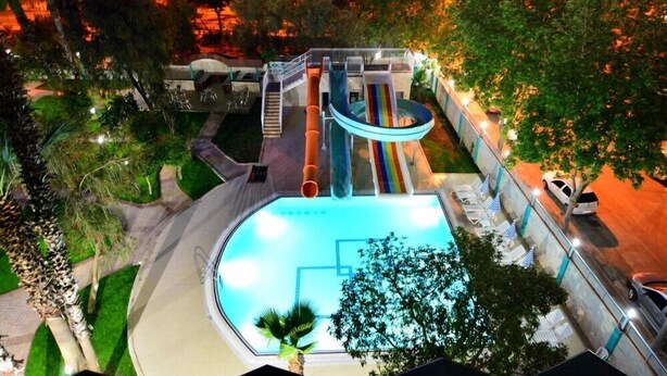 Une piscine extérieure avec un toboggan, entourée d’arbres et bordée d’une allée pavée.