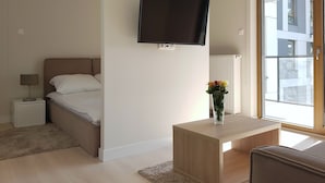 A modern hotel room with a bed, bedside table, lamp, TV, and a window with a view of buildings. - Chopin Apartments Union (Warsaw)