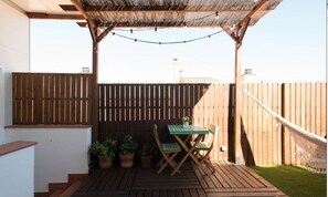An outdoor patio area with a wooden deck, a table and chairs, potted plants, and a pergola with string lights. - Gaudint Barcelona suites (Barcelona)