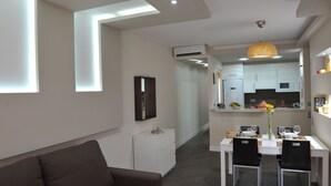 Una sala moderna con sofá, un comedor con mesa para dos y una cocina al fondo.