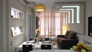 Un comedor moderno con una mesa blanca dispuesta para cuatro personas, un sofá marrón y una lámpara decorativa en el techo.