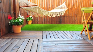 Una terraza de madera con una hamaca y plantas en macetas.