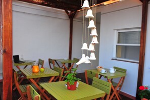 An outdoor patio with green tables and chairs, a hanging bell decoration, and a window in the background. - Gaudint Barcelona suites (Barcelona)