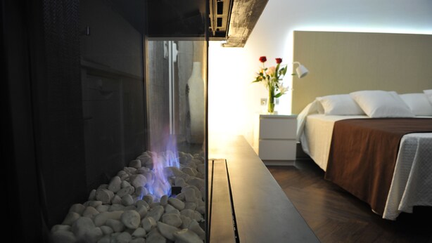 Una habitación moderna con chimenea de piedra, una cama bien tendida y una mesita de noche con un florero.