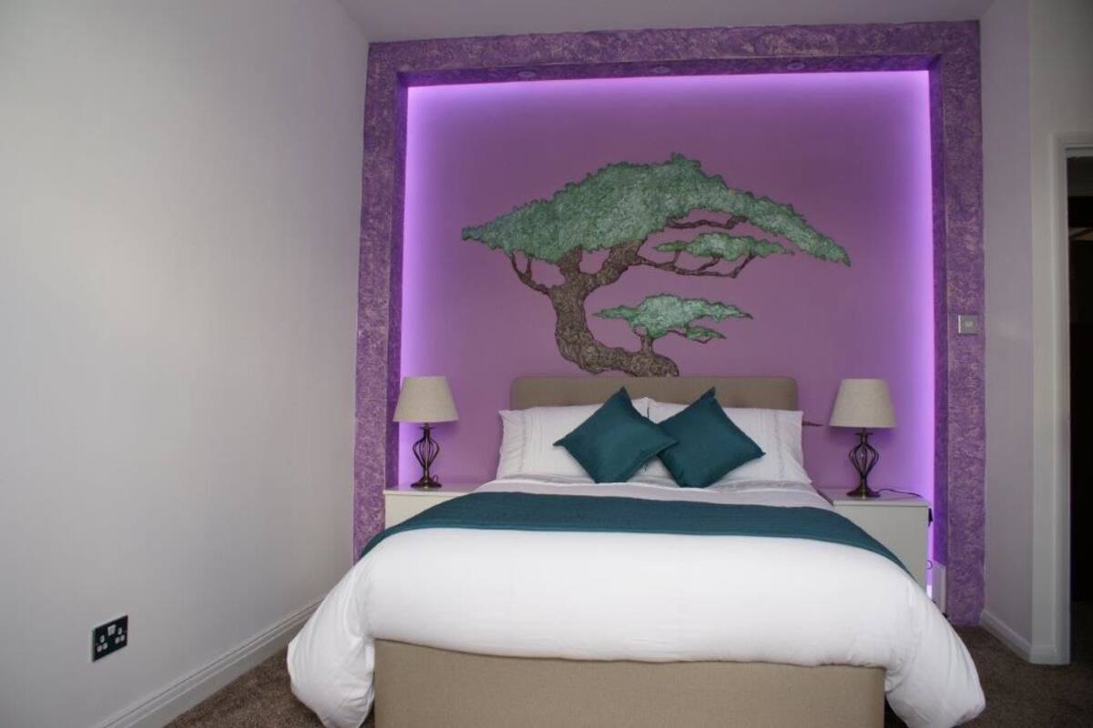 Ein Schlafzimmer mit einem Bett, zwei Nachttischen und einem an der Wand hängenden Baum-Kunstwerk.