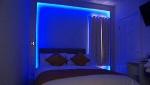 A bedroom with a bed, curtains, and a nightstand. - LG Thai Derm Spa & Guesthouse (Loughborough)