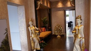 A hallway with two golden statues, a bench, and a decorative tree. - LG Thai Derm Spa & Guesthouse (Loughborough)