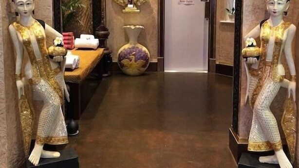 A reception area with two mannequins in traditional attire, a decorative vase, and a sign indicating the entrance to the spa. - LG Thai Derm Spa & Guesthouse (Loughborough)