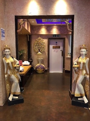 Un espace d’accueil avec deux mannequins vêtus de costumes traditionnels, un vase décoratif et un panneau indiquant l’entrée du spa.