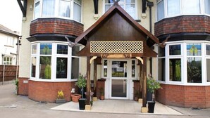 A corner building with a bay window entrance, a welcome sign, and potted plants. - LG Thai Derm Spa & Guesthouse (Loughborough)