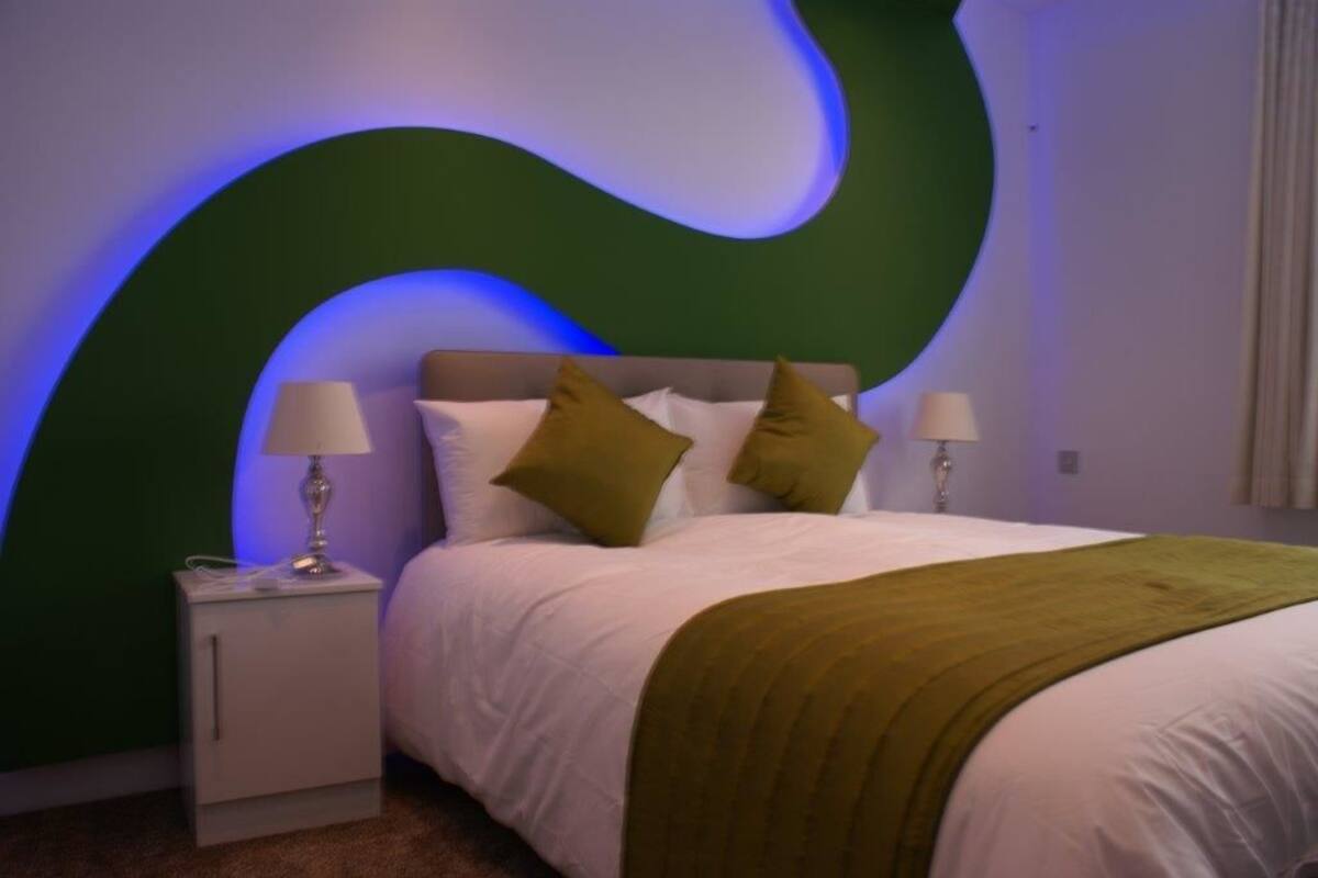 Ein modernes Schlafzimmer mit einer gewölbten grünen Wand, einem weißen Bett mit grüner Tagesdecke und zwei Nachttischlampen.
