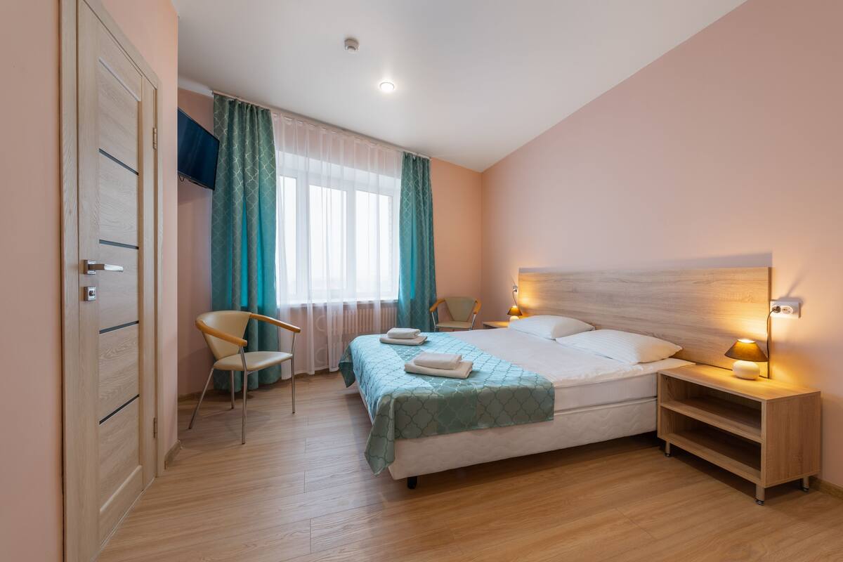 A bedroom with a bed, a chair, a nightstand, and a TV.