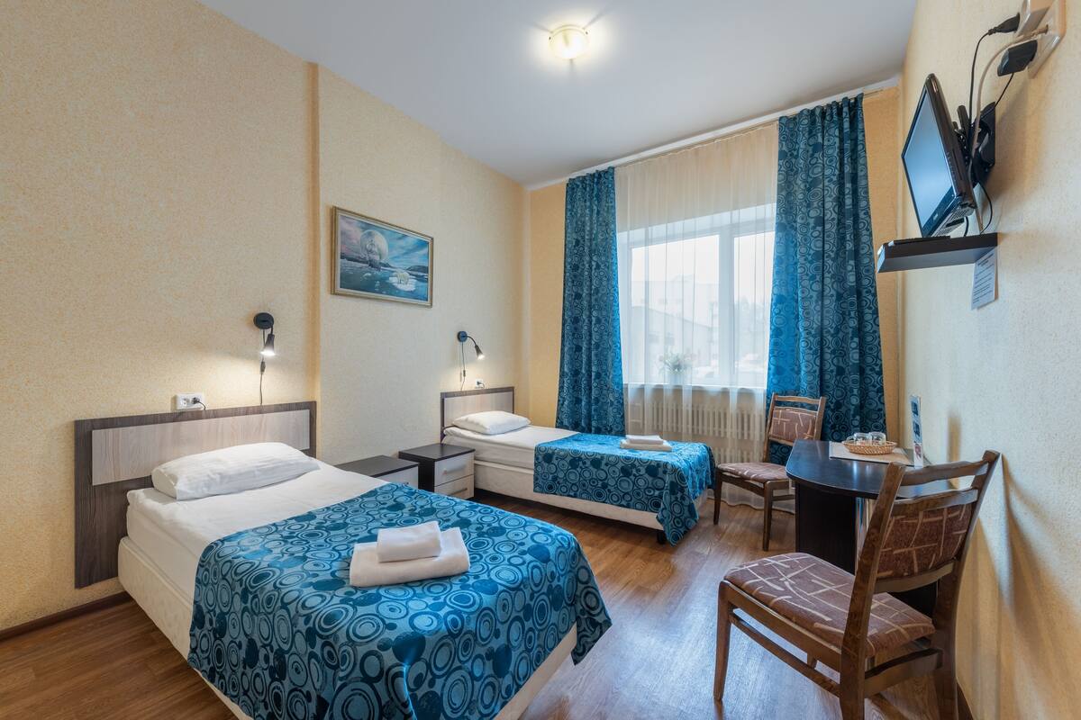 A hotel room with two beds, a desk with a chair, a television, and a window with curtains.