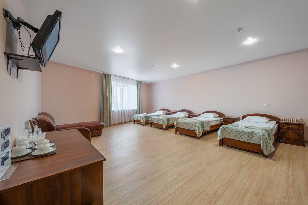 A hotel room with four single beds, a wooden desk with a television, and a dining area with chairs and a table set for four.