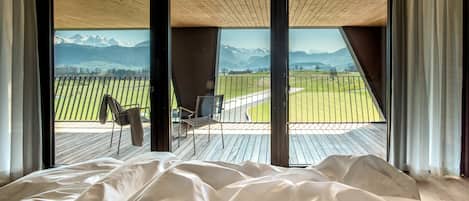 A bedroom with a large bed and a view of a balcony with a chair and a table.